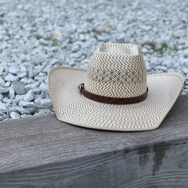 Two S Leatherwork Wave to the Crowd Hat Band on a straw hat, sitting on a wall edge with stones behind.