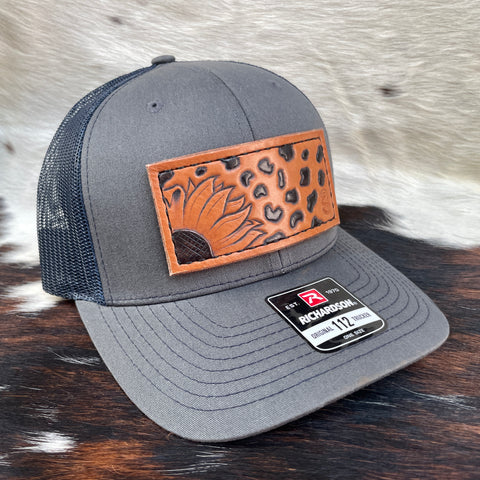 Charcoal Grey/Navy Blue Richardson 112 Trucker Hat with hand carved sunflower and leopard print patch, hand dyed, and hand stitched. Front.